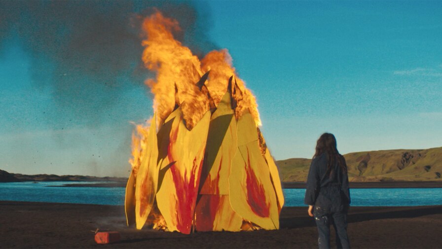Still from Forever Love: A woman stands next to a fire in front of a lake.