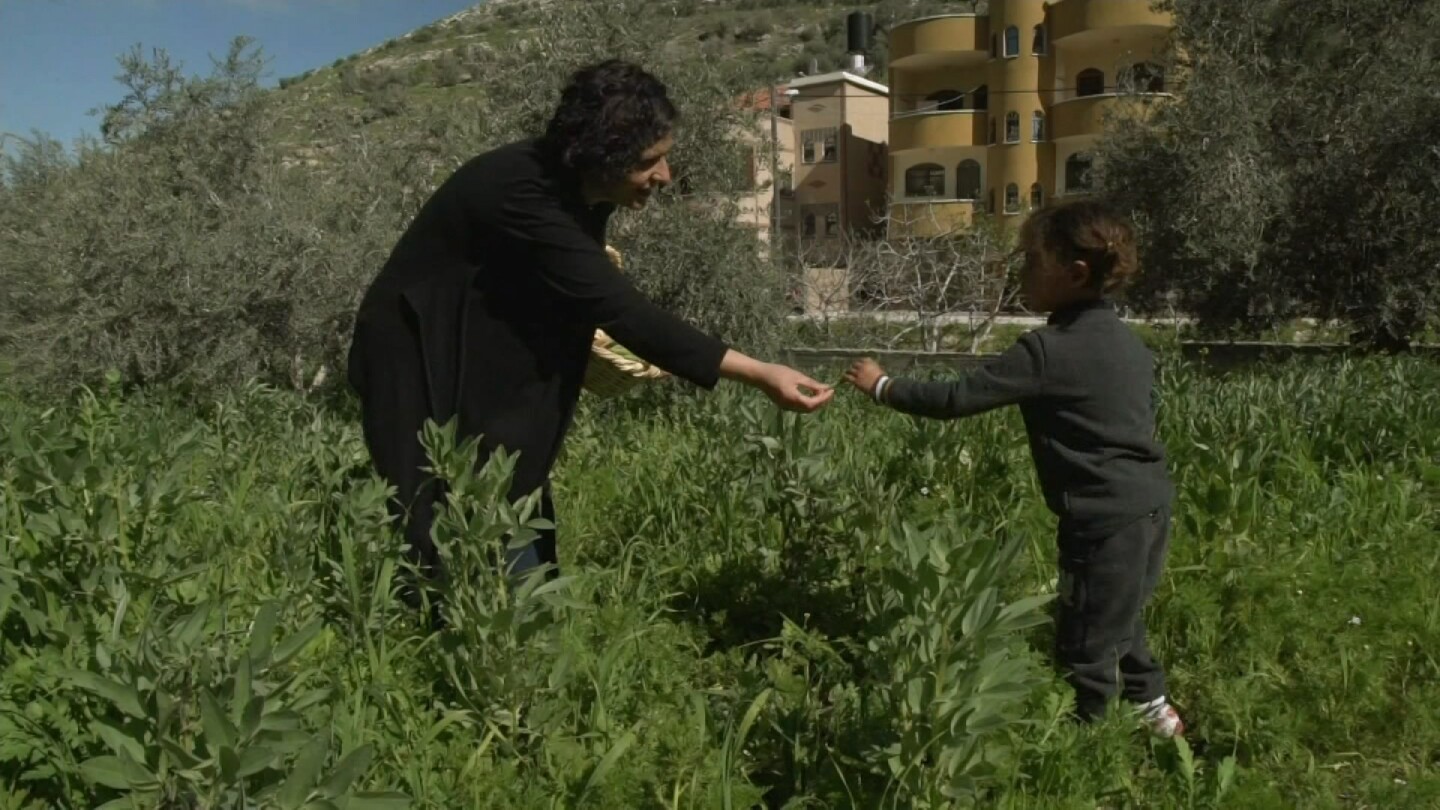 Woman in a garden hands something to a young girl. | Still from "Witness" episode "The Seed Queen"