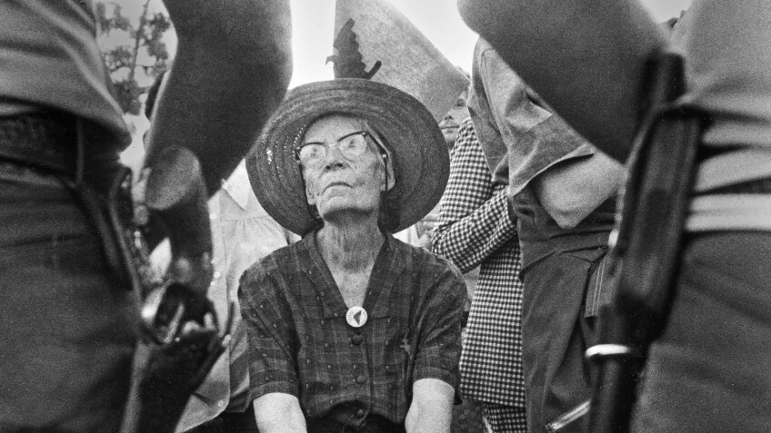 Dorothy Day is seated within a crowd of standing people. | "Revolution of the Heart: The Dorothy Day Story"