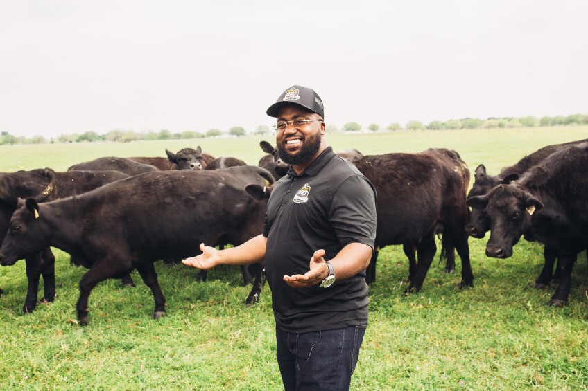 A man wearing a black outfit stands in front of a herd of cattle.
