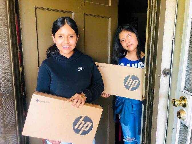 Two young girls pose in a doorway, each holds a laptop box.