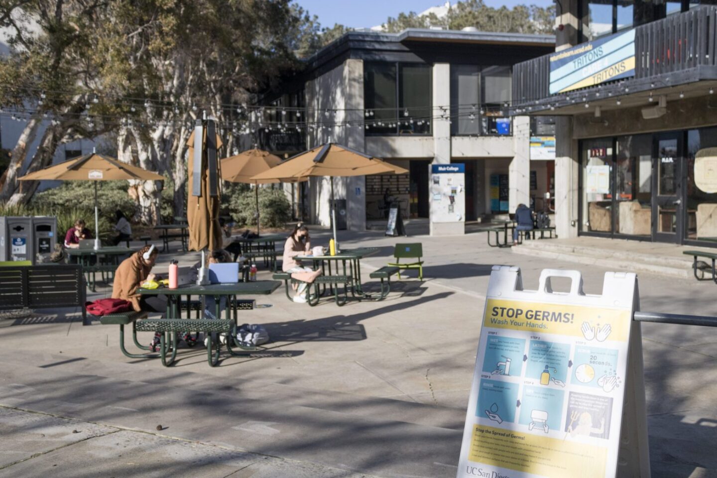 Students study outdoors in Muir Quad at UC San Diego on Feb. 17, 2021. A sign outlines the correct hand-washing procedures to fight COVID-19.