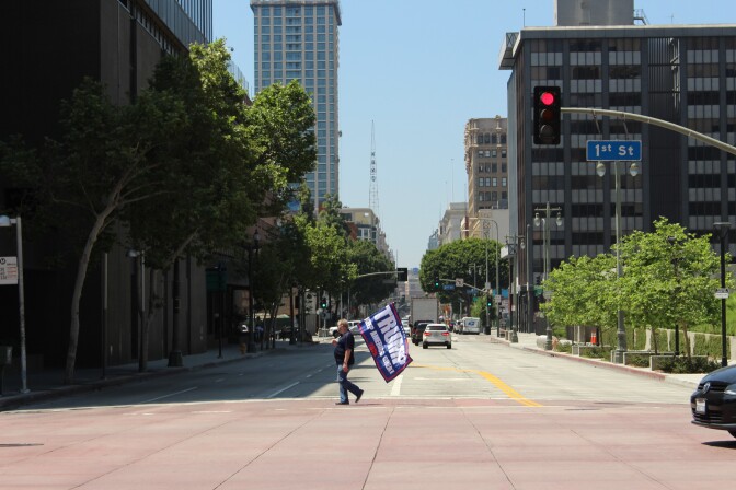 Man crosses the street in Downtown L.A. with "Trump 2020" flag in hand | Karen Foshay