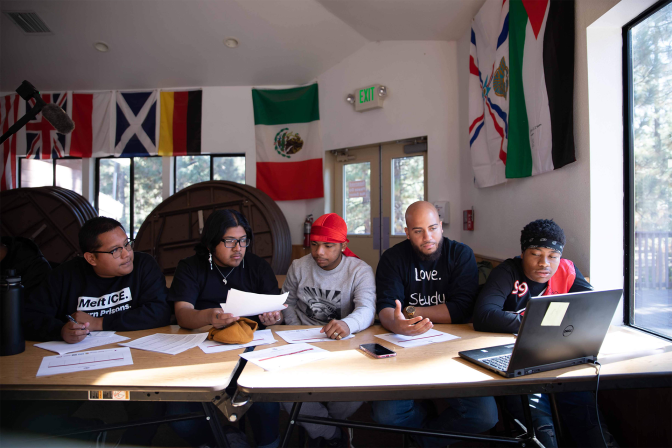 5 men sit at a table in front of a laptop
