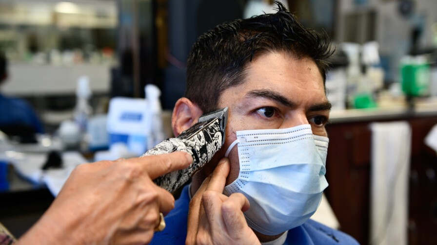 Carlos Hernandez holds his face mask while getting a haircut during the pandemic.