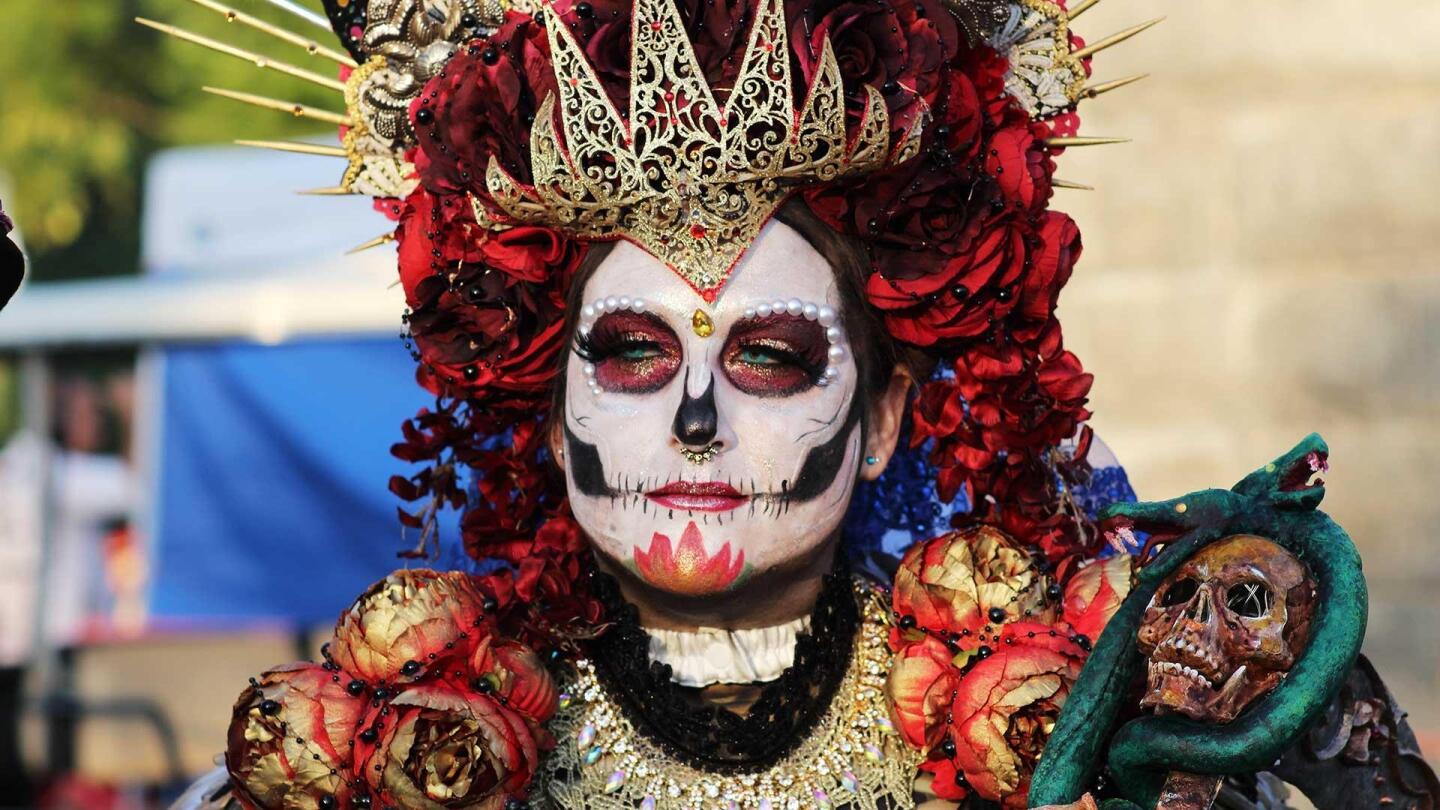 A photo of someone dressed vibrantly and wearing intricate face painting for Día de Los Muertos.