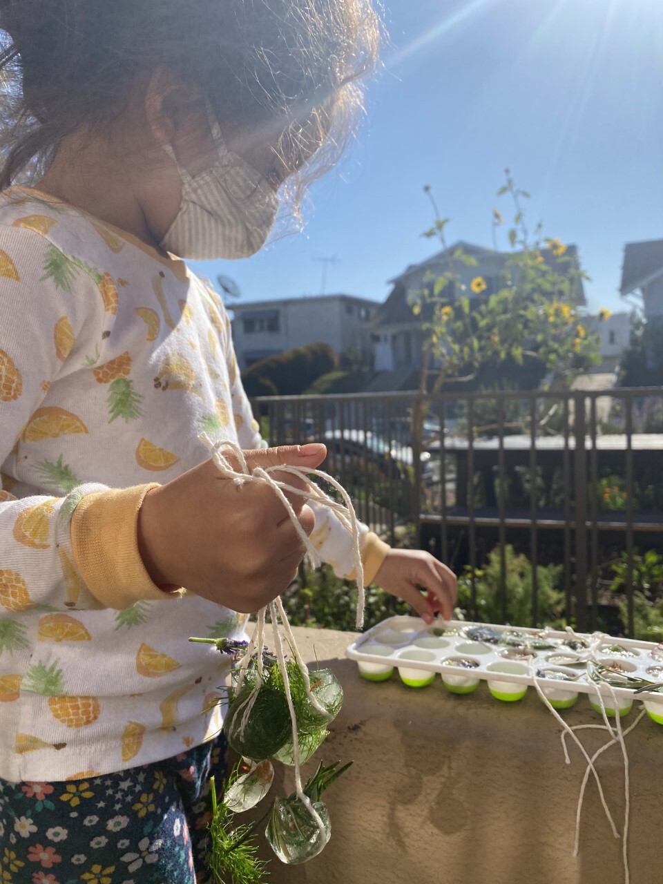 A toddler pulls out frozen green plants on a strong from an ice tray.