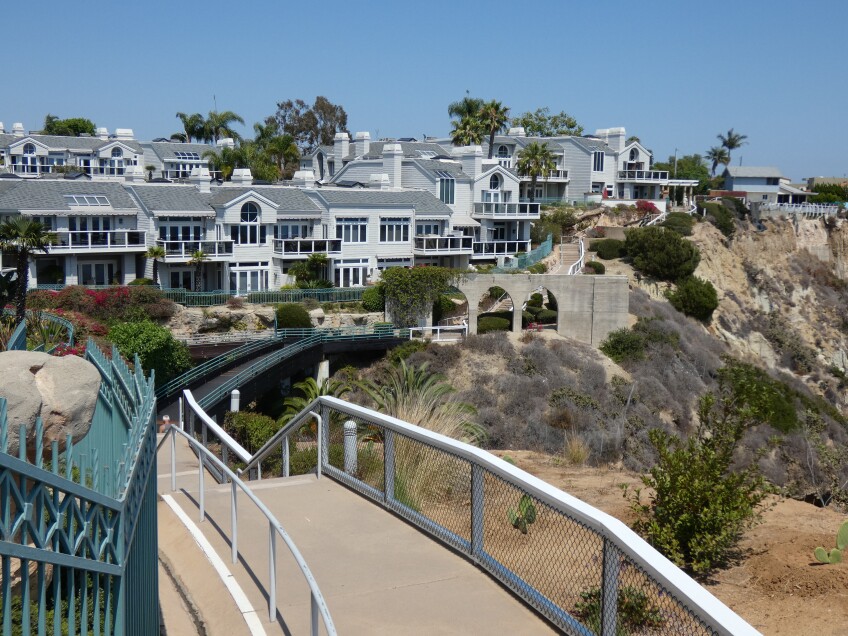 A paved walkway stretches along a coastal cliff lined with white residential homes. 