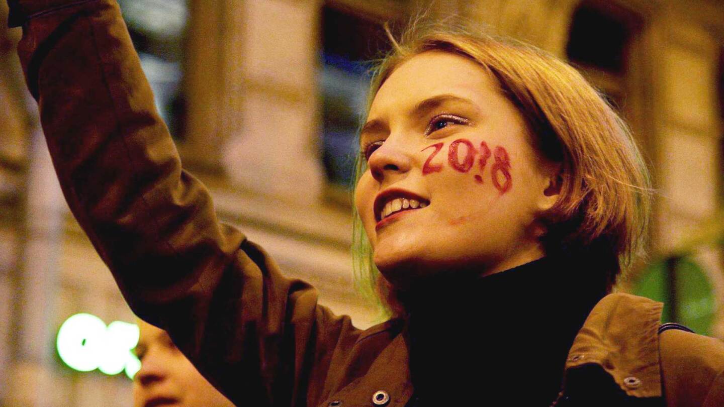 Blonde woman with "2018" face painted across her face. | Foreign Correspondent featured image