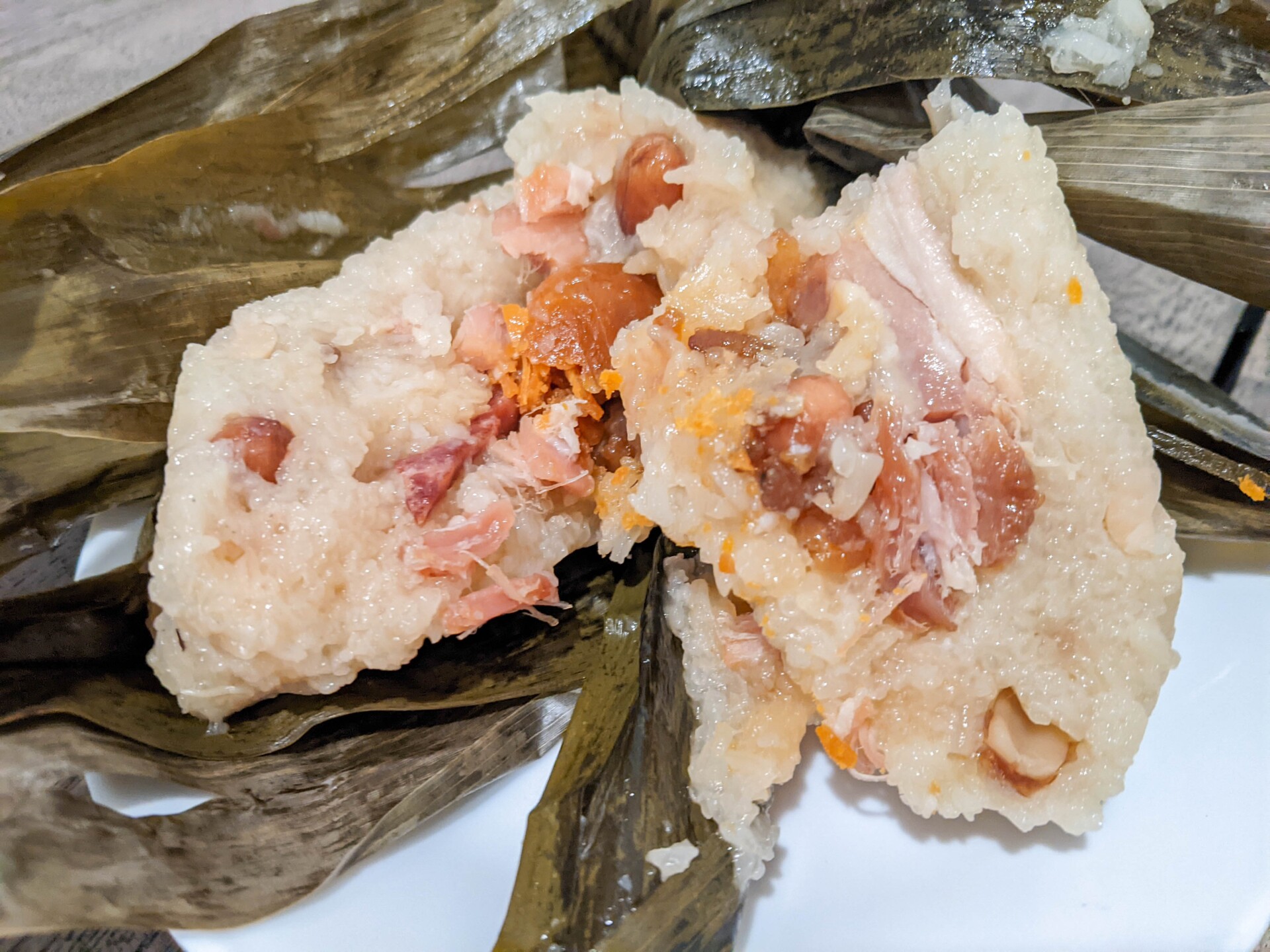 Sliced chicken and marinated in sticky sauces inside of a sweet rice form the tamale. The tamale is cut in half and sits on banana leaves.