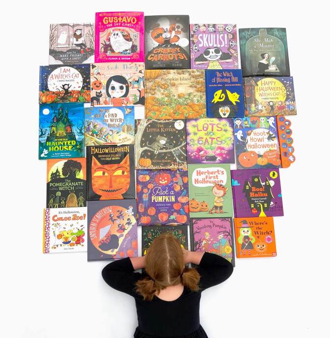 View of a little girl from above as she looks over 23 books arranged on the floor.
