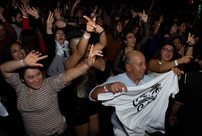 A crowd dances at the Cumbiaton Posada Tropical event December 28, 2020. A man in the foreground holds up a white t-shirt that reads, "Cumbia."