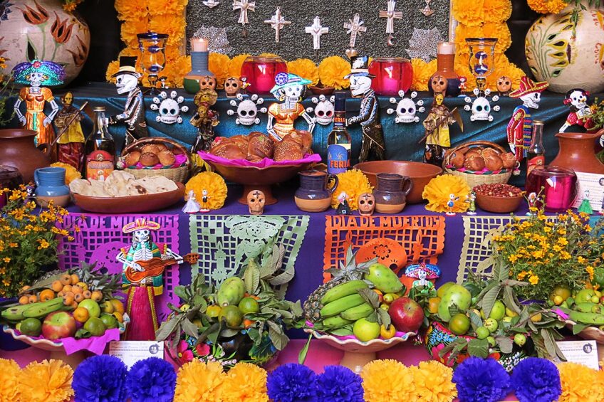 A Day of the Dead altar is covered in flowers, bread, decorative skulls and intricately cut brightly colored paper.