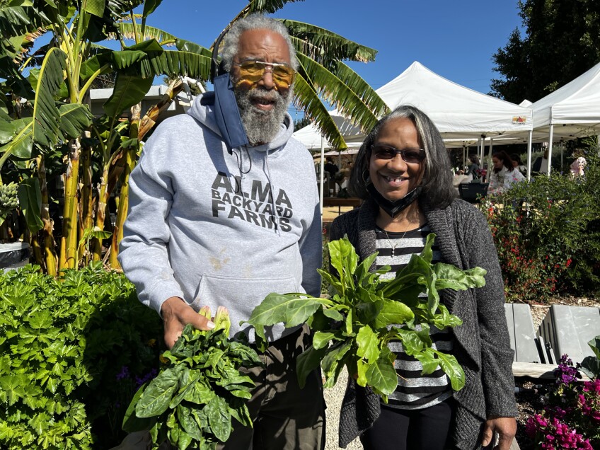  alma backyard farms a Black couple stand smiling as they hold vegetables