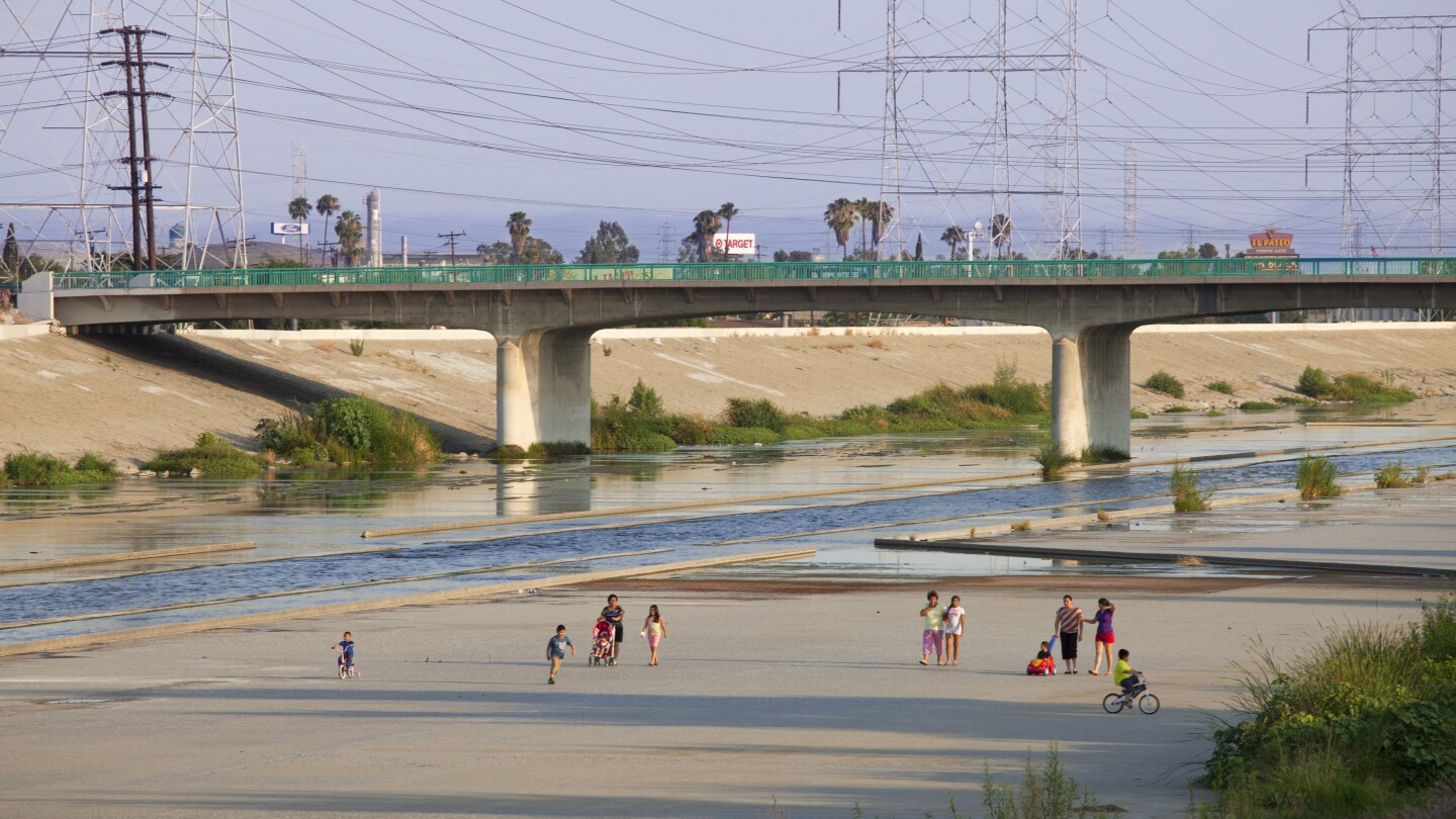 A wide shot of families walking along the concrete banks of the LA river with a bridge in the background