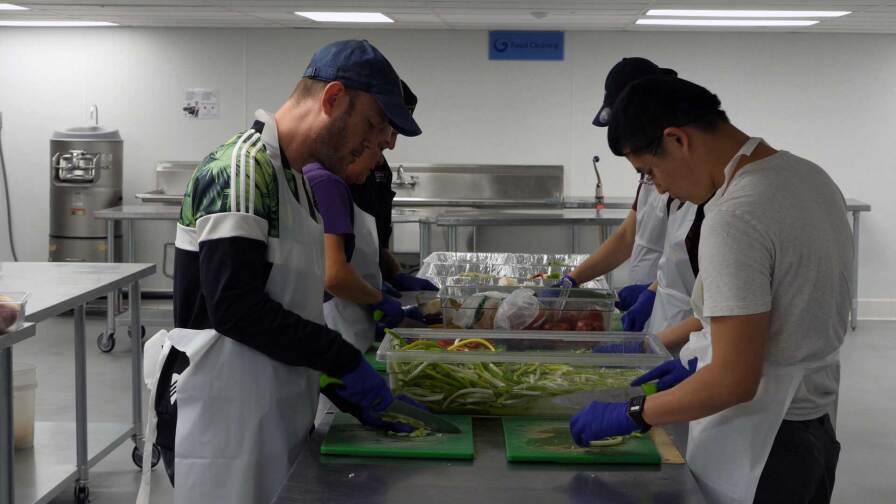Participants of L.A. Kitchen's food culinary training program chop vegetables. Still from video by Chase Alexander