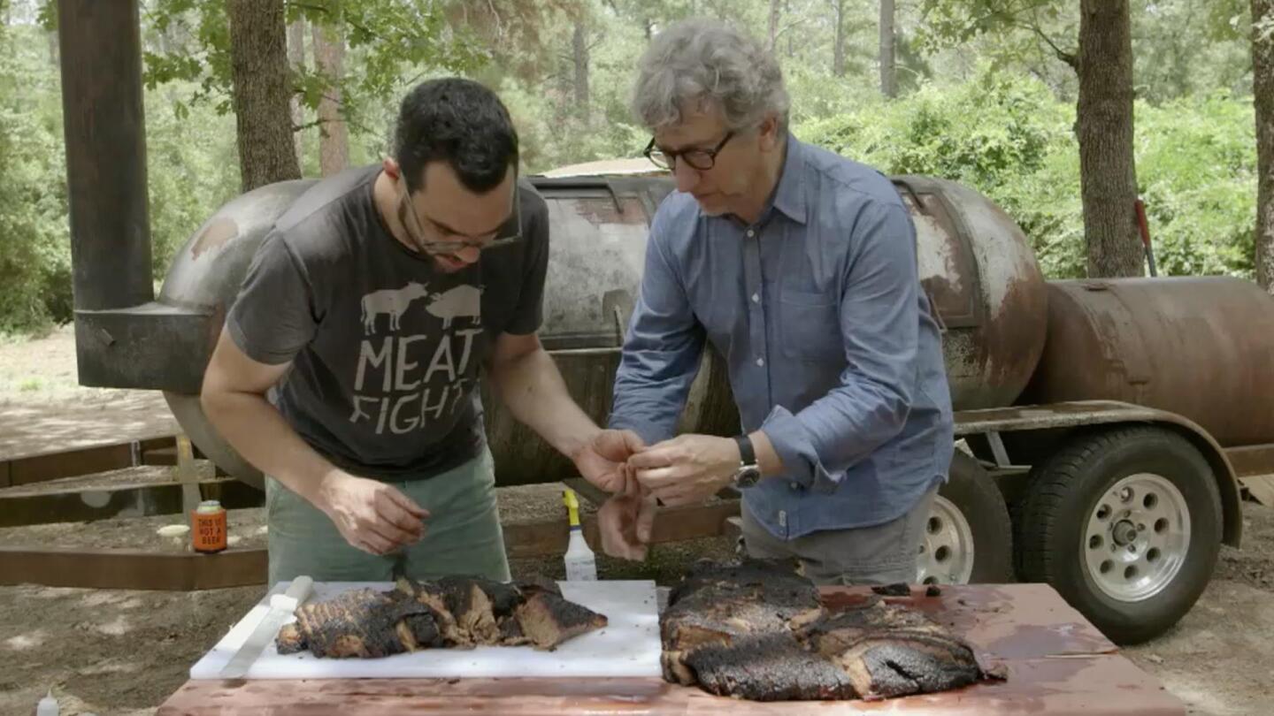 Two men prepare slabs of smoked brisket.