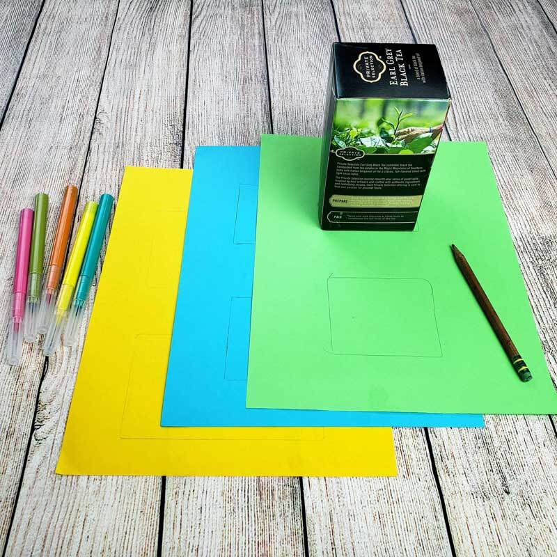 Materiales de manualidades, que incluyen una caja pequeña, marcadores y papel de construcción son colocados sobre una mesa.