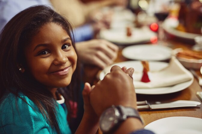 Portrait of an adorable little girl holding hands in prayer with her family before having a meal together. iStock