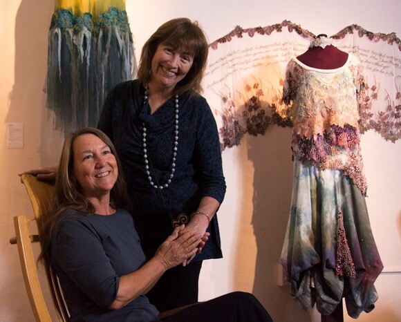 Melinda Forbes and Julie Frankel organized the exhibition "Earth Gowns: Narrative Dresses, Stitched Storytelling" at the Steynberg Gallery in San Luis Obispo. In the background is "Rooted in Beauty" by Mary Wood. | Chris Daly