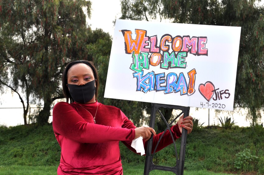 Kiera Newsome poses with her welcome home sign, wearing a protective face mask from her family | Gina Pollack