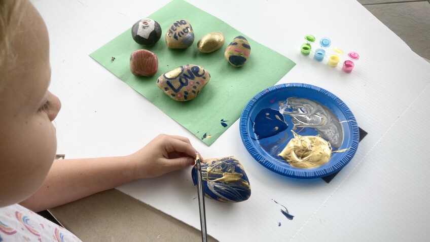 A small child paints an abstract pattern on a rock.