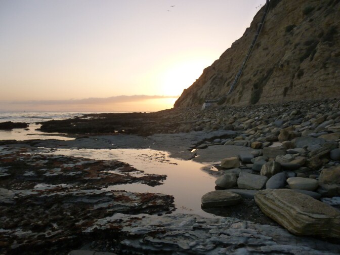 A sunset shines a warm glow on an almost dry shore of Cabrillo Beach in San Pedro.