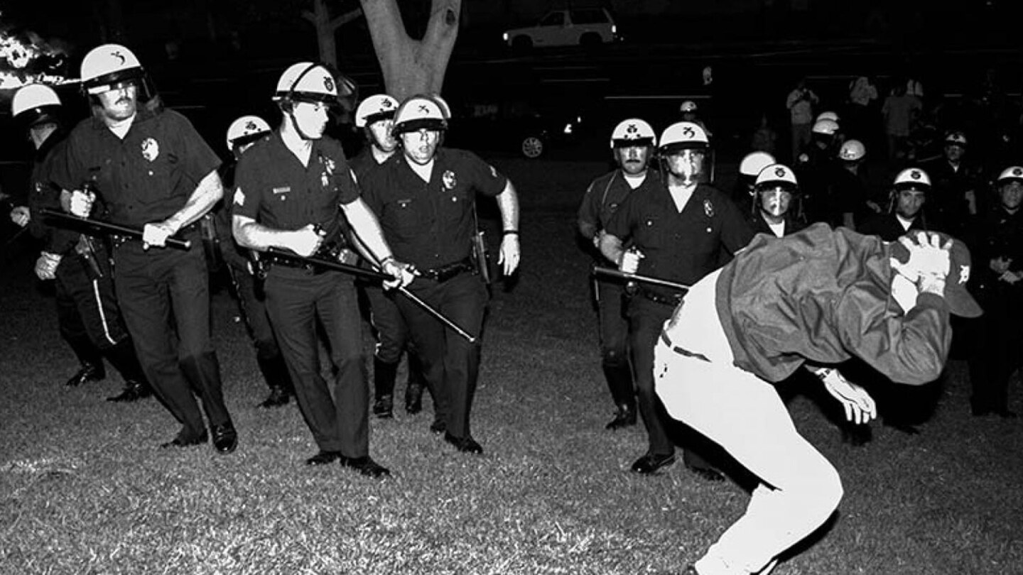 Los Angeles, 1992: Scan from negative of LAPD officers from Parker Center advance across City Hall lawn against stricken rioter in the early evening