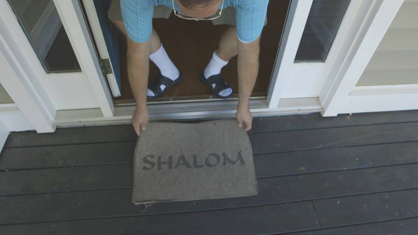 Terence places “Shalom” Welcome Mat at new home. | Photo credit: 371 Productions