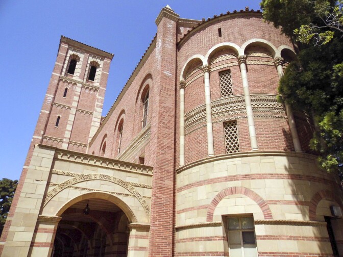 A side view of the Royce Hall building on UCLA's campus. The building is predominantly made of red bricks, with cream/beige bricks incorporated in some areas decoratively.