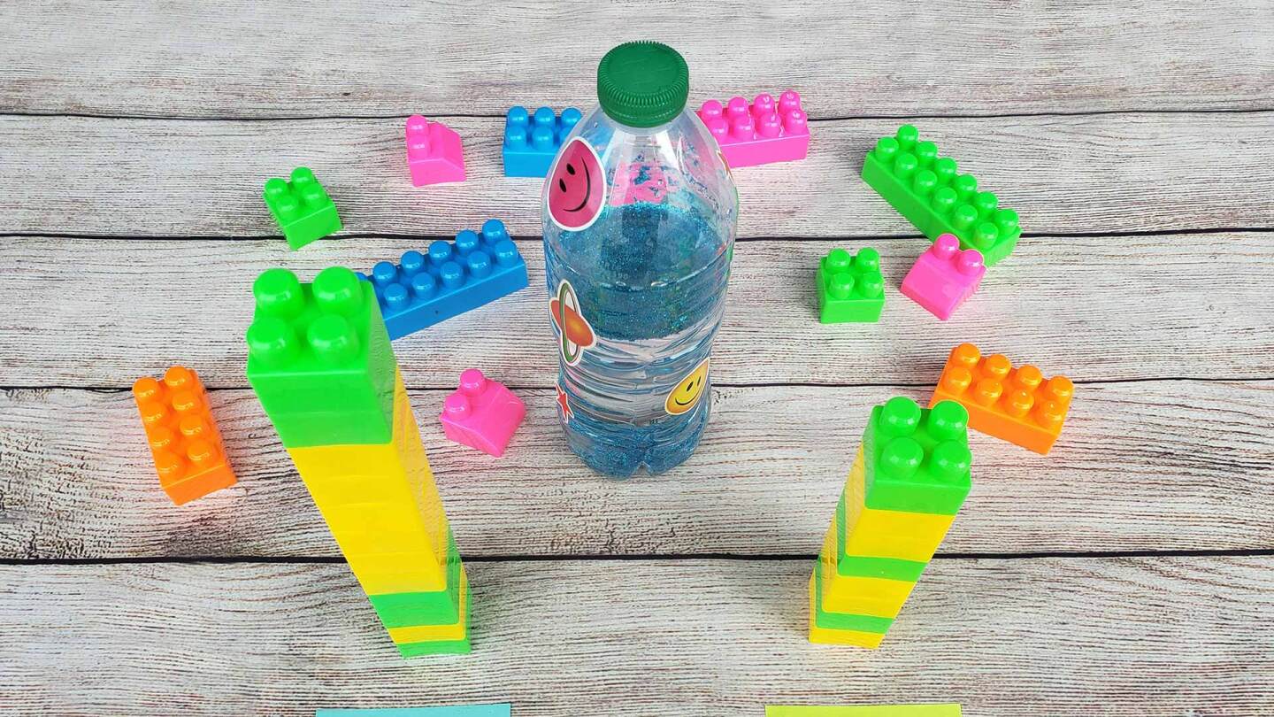 A water bottle with sparkly blue water stands alongside colorful plastic blocks in two towers and two post-its labeled "stands" and "falls."