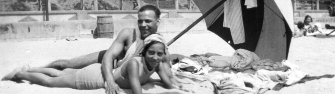 A minority couple laying on the beach together under an umbrella