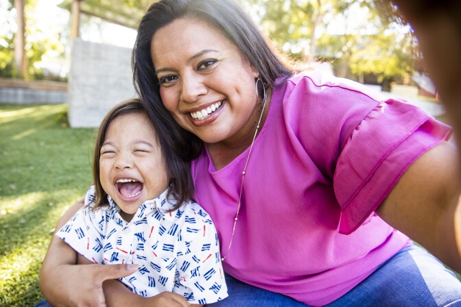 A young mother takes a selfie with her son, who has Down syndrome, in the park.