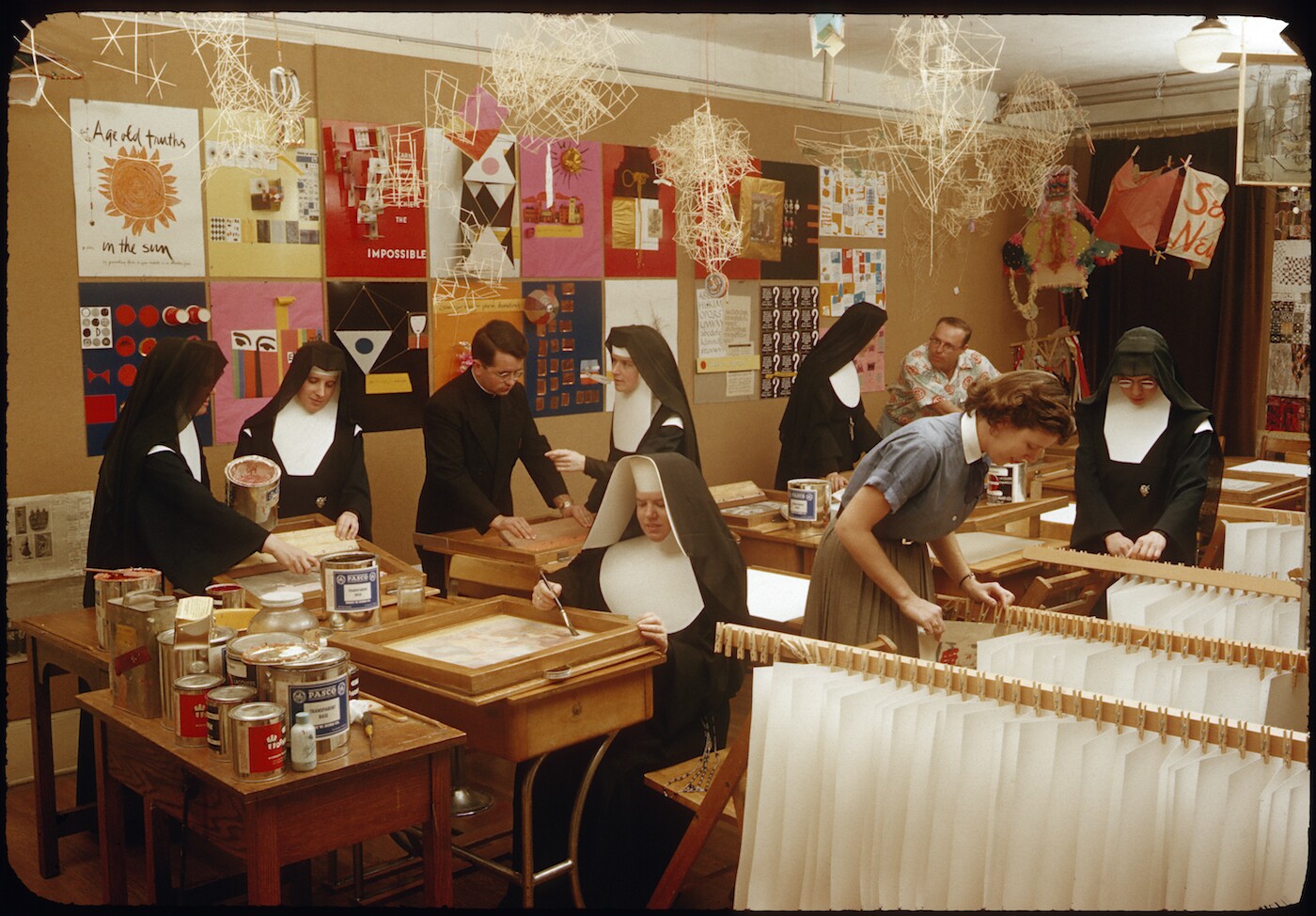 Educators at Immaculate Heart College, many are wearing nun's habits. Art line walls and hang from the ceiling.