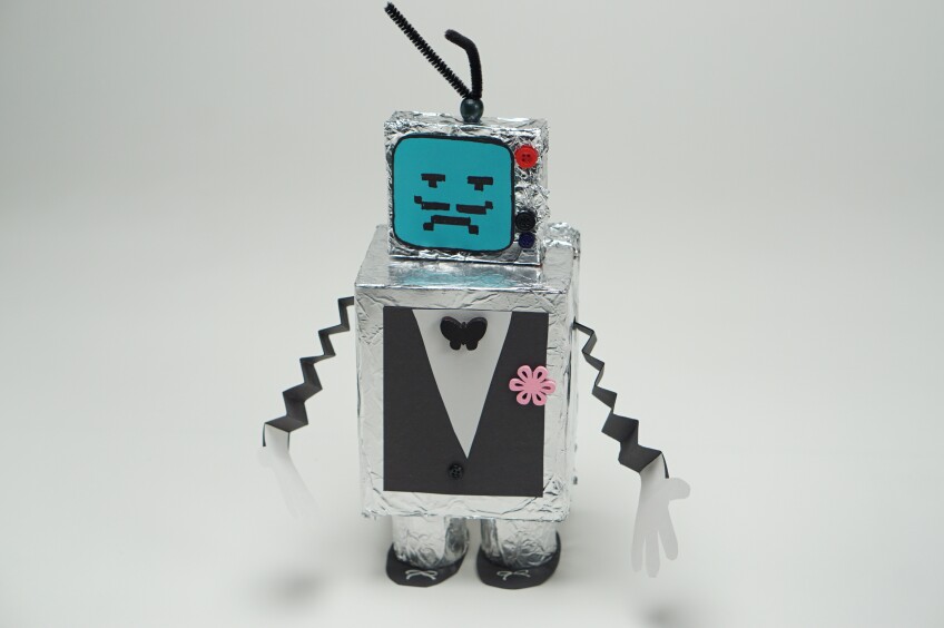 a mustachioed robot craft made out of boxes covered in aluminum foil decorated with paper decorations made to resemble a suit.