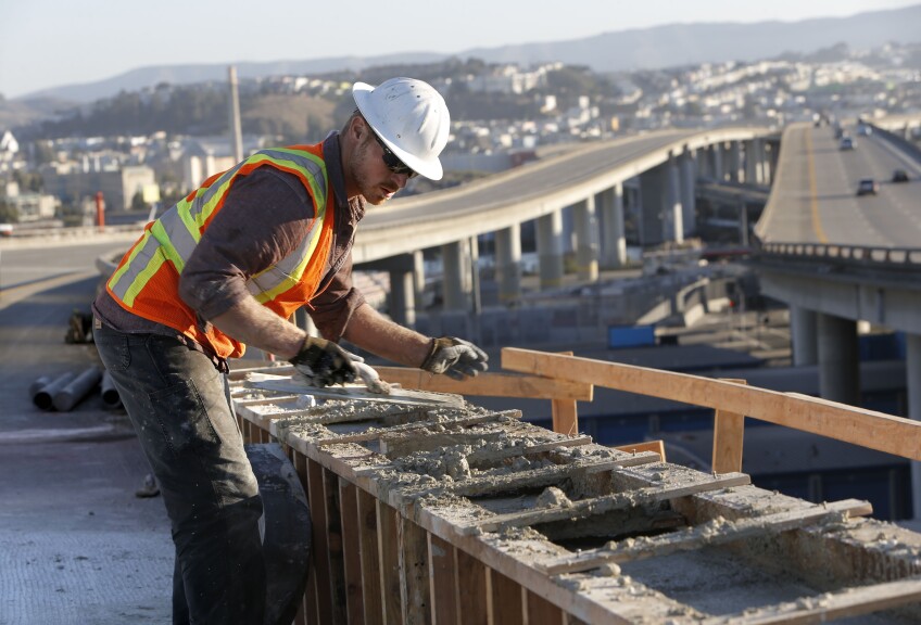 a man in a hard hat smooths concrete with a highway in the background