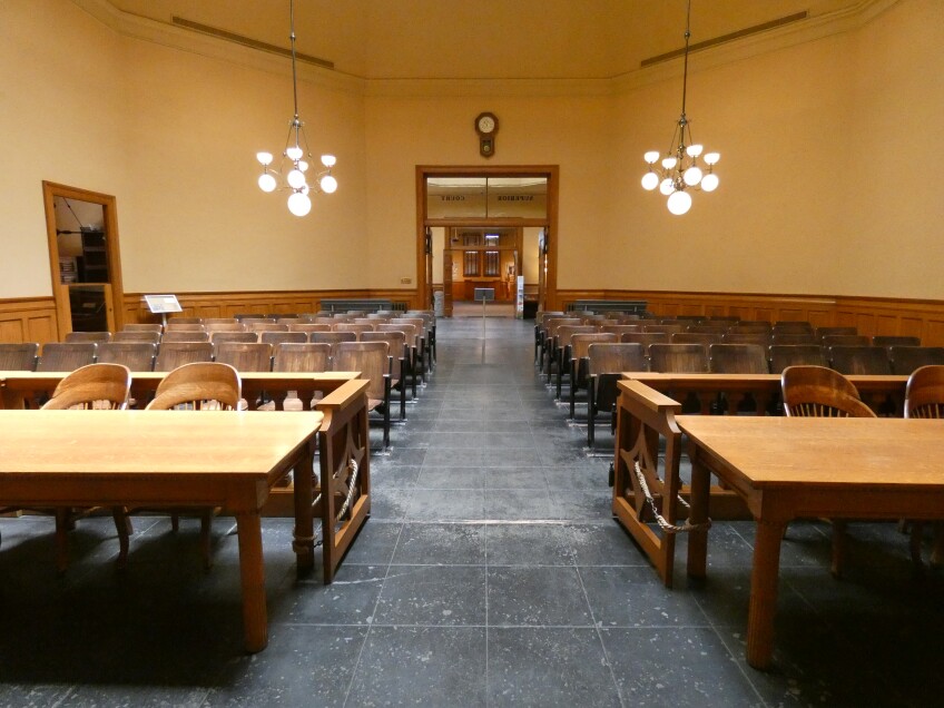 A historic Superior Courtroom filled with oak audience seating and tables and with period chandeliers hanging off the high ornamented ceiling. 