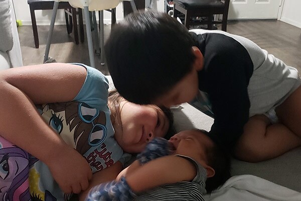 Three smiling children cuddle together.
