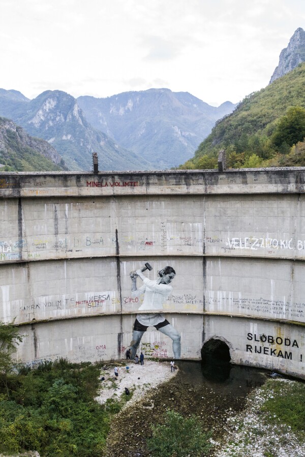 a large damn with graffiti of a woman with a hammer on it, mountains in the background