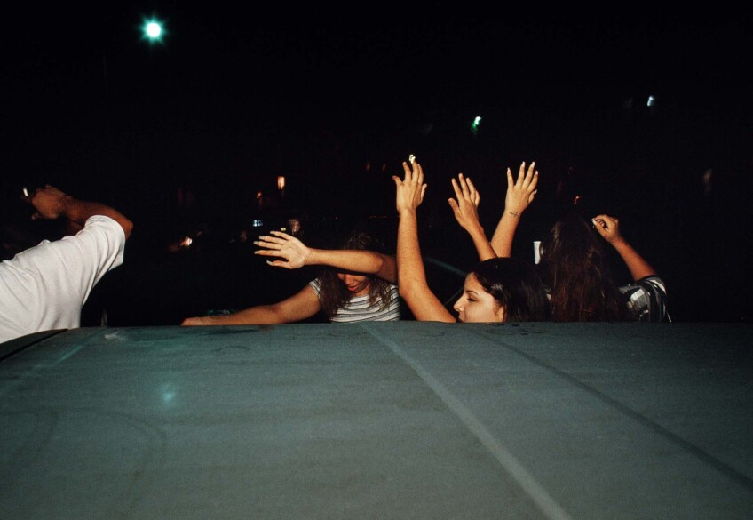 Young people in Pico-Union are photographed with their hands raised behind a car at night. 