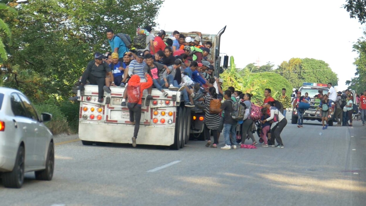 Dozens of migrants hopping onto the back of a truck. | Still from Global Mosaic