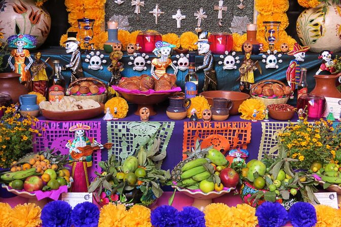 A Day of the Dead altar is covered in flowers, bread, decorative skulls and intricately cut brightly colored paper.