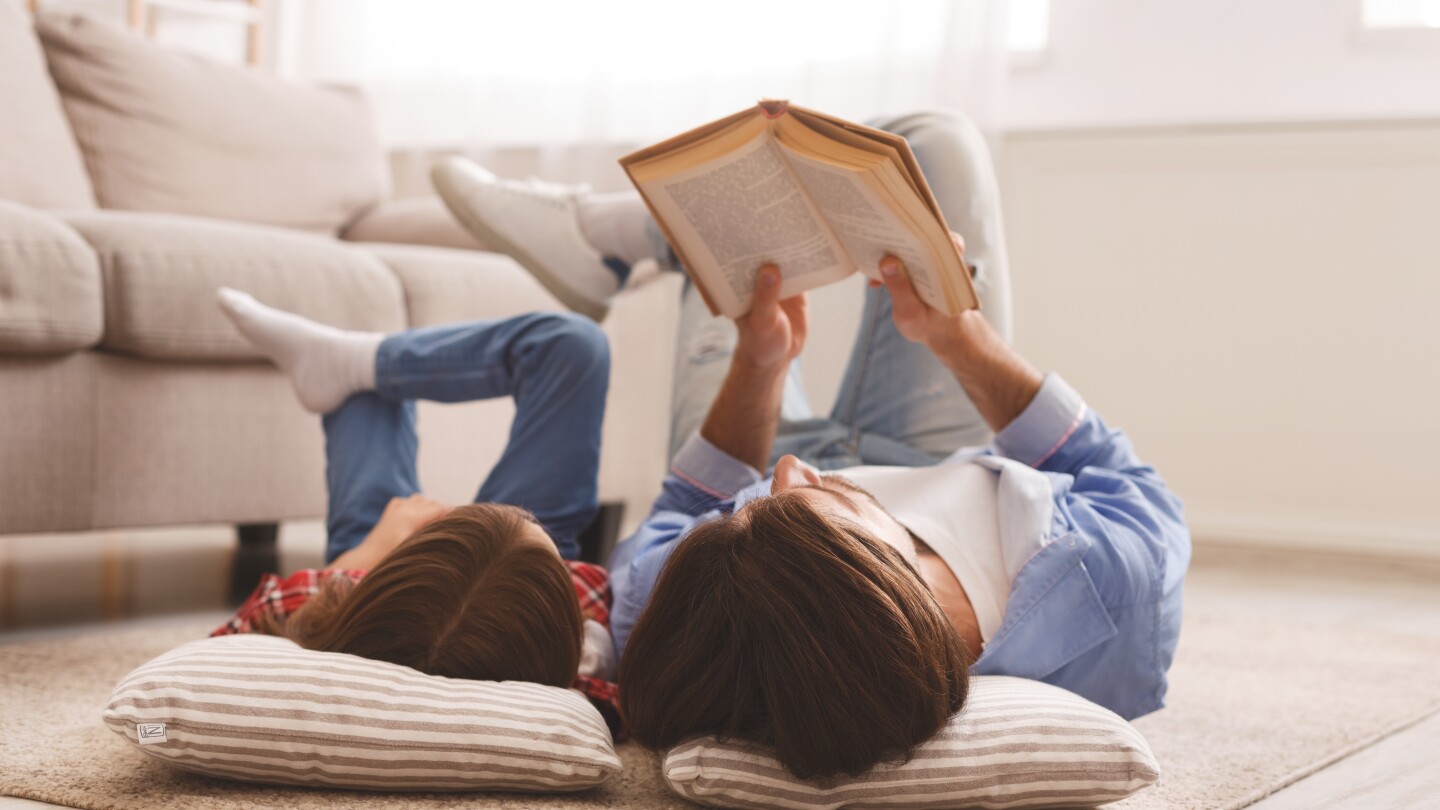 Little girl and father enjoying book together, laying on floor