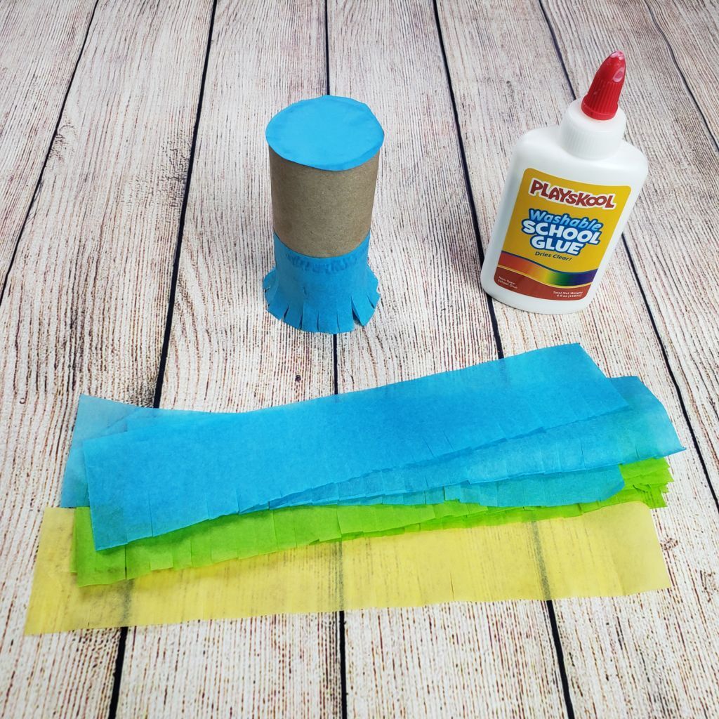 Se pegan trozos de papel crepé de colores cortados desde la parte inferior para formar un fleco en un rollo de papel higiénico vacío.