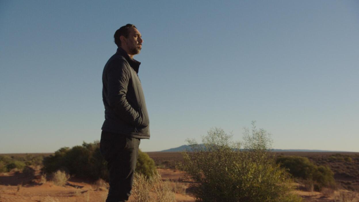 A man with his hands in his pockets looks out to a vast landscape.