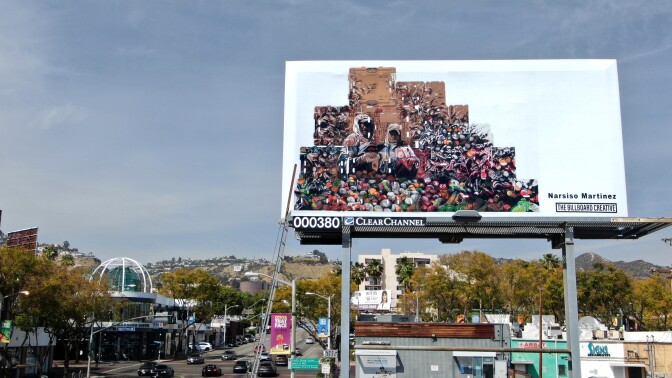 A billboard shows two farmworkers superimposed against piles of produce and the wooden crates used to transport them.