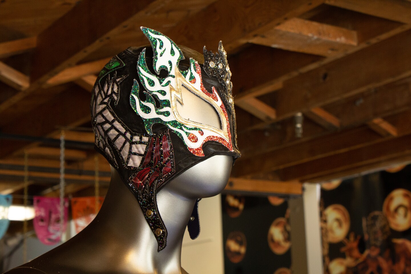 A lucha libre mask is worn by a mannequin with sequins and with green, gold and red colors.