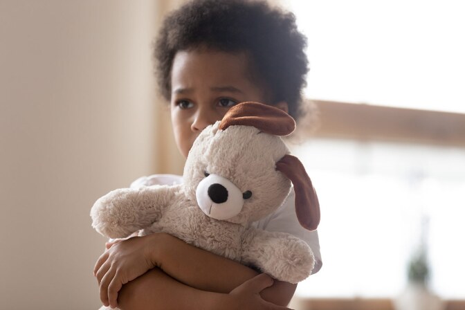 A sad-looking little boy hugs a stuffed dog tightly. iStock