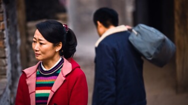 A woman looks sorrowfully aside as a man walks away behind her. | From "Mountains May Depart"