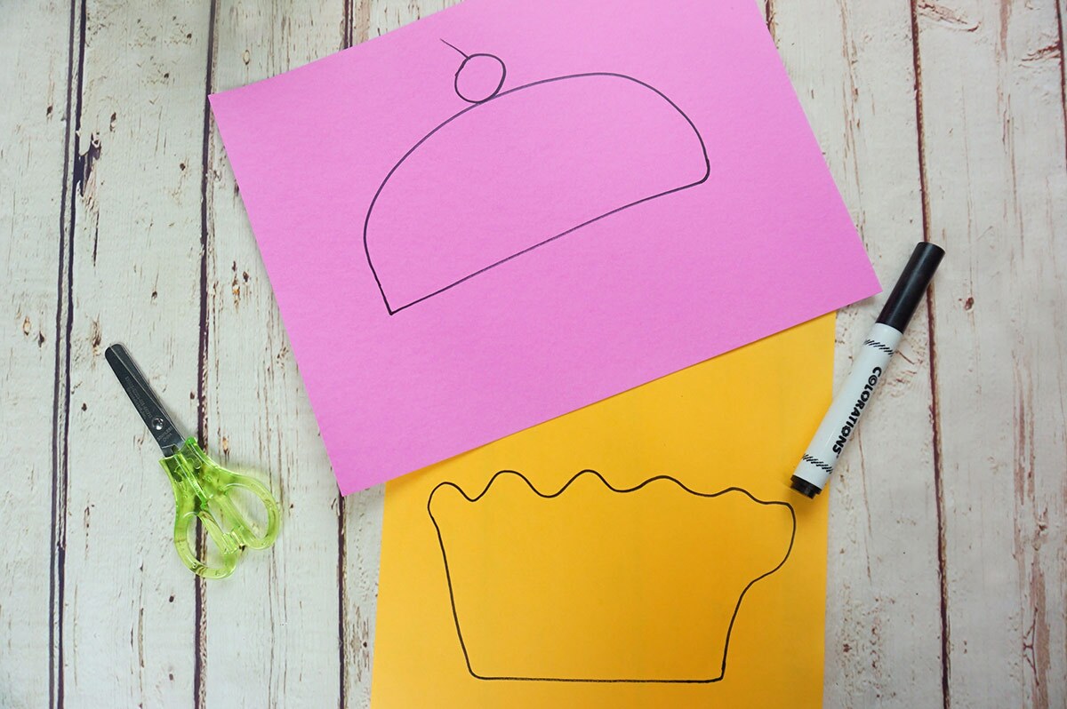 Two pieces of paper, one pink and one orange, with the top and bottom parts of a cupcake drawn on them.